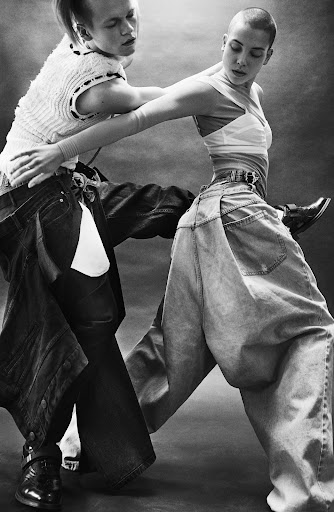 Two fashion models in dramatic pose wearing baggy denim pants in a studio, showcasing alternative and streetwear fashion trends.