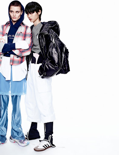 Two fashion models pose in an indoor studio setting wearing contemporary outfits with contrasting colors. The models are side-by-side.