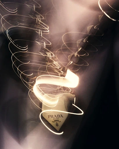 Prada logo pendant on a necklace with light painting trails in a studio setting. Fashionable jewelry item with dynamic light effects.