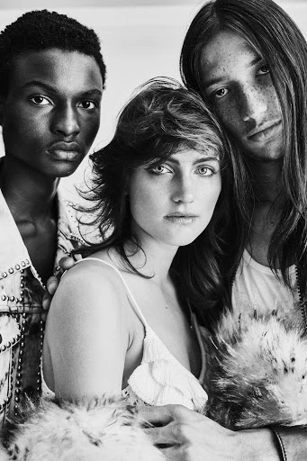 Three diverse models pose together in a black and white studio shot. A woman in the center is flanked by two other models. 