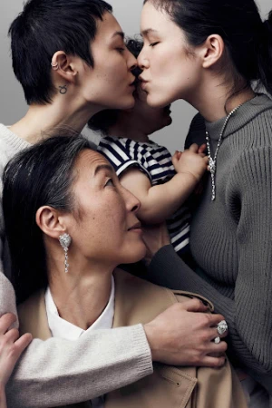 Three generations of women including an Asian grandmother, mother, and daughter embrace while showcasing fine jewelry in a neutral studio.