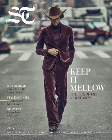 Magazine cover featuring a male fashion model in a brown velvet suit and hat, walking on a city street with traffic in the background.