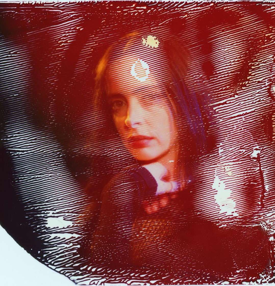Portrait of an adult woman with light skin, framed by dark red colors, and abstract lines, creating an artistic, blurred effect.