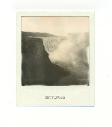Sepia toned landscape photograph of Dettifoss waterfall in Iceland. The powerful falls send up mist near dark cliffs, captured in analog style.