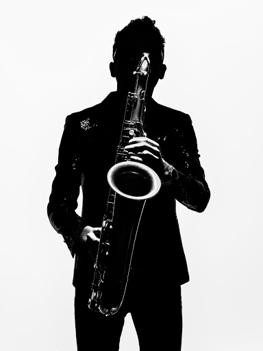 Silhouette of musician in sequin jacket playing saxophone against white background. Black and white studio shot showcases musical performance.
