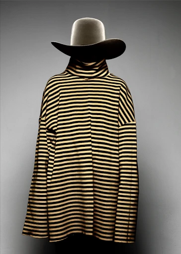A striped sweater and hat are displayed on a mannequin against a grey background. The presentation highlights fashion apparel.
