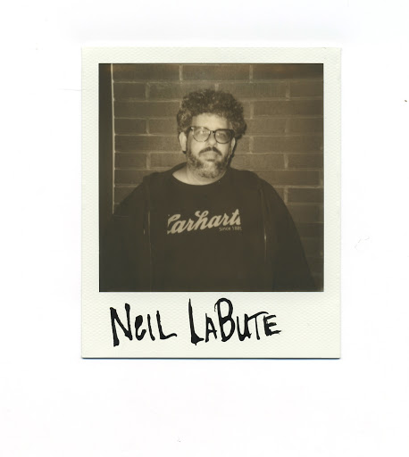 Portrait of adult male with glasses wearing a Carhartt sweatshirt in front of a brick wall, captured in a Polaroid-style photograph.