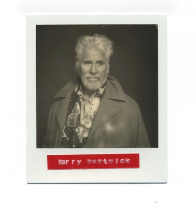 Polaroid portrait of Barry Bostwick wearing a dark coat and patterned scarf with a red label below the frame