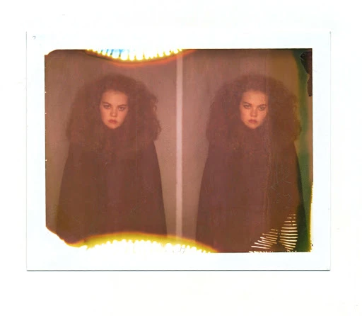 Double exposure portrait of a young woman with dark curly hair wearing a black cloak in a photo studio with soft, moody lighting.