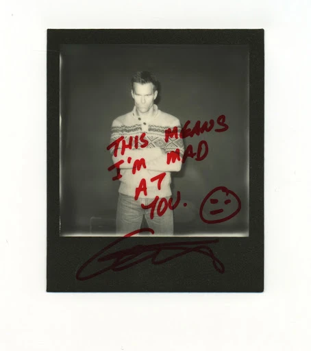 Monochrome Polaroid of a man in a fair isle sweater with arms crossed, featuring hand-written text and signature on the print.