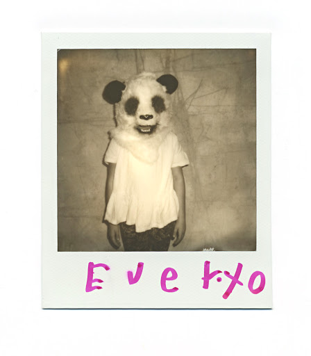 Child in a panda mask and white t-shirt stands in front of a wall in a square sepia-toned photograph with pink text on the frame.