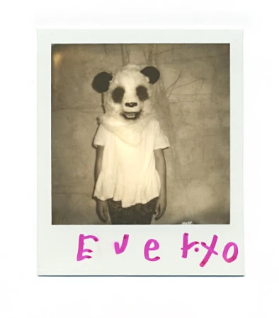 Child in a panda mask and white t-shirt stands in front of a wall in a square sepia-toned photograph with pink text on the frame.