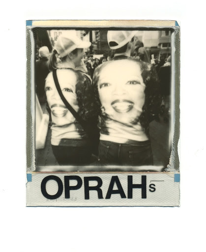 Black-and-white photo featuring two adults wearing T-shirts printed with a portrait, captured amid a crowd during an outdoor daytime event.