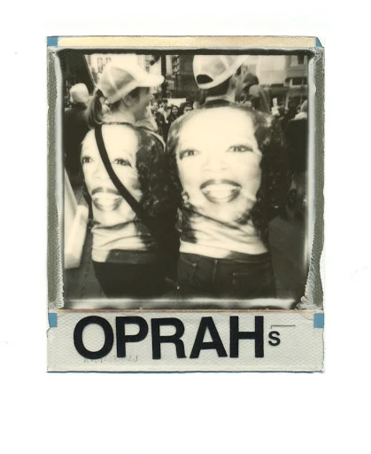 Black-and-white photo featuring two adults wearing T-shirts printed with a portrait, captured amid a crowd during an outdoor daytime event.
