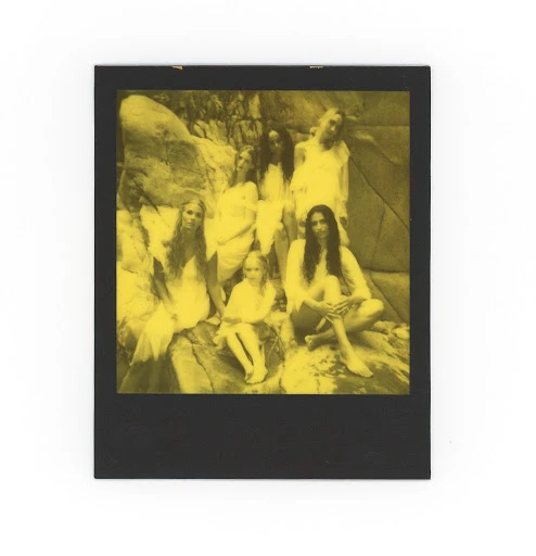 Group portrait of seven women and one child in white dresses posing on rocks in a monochrome outdoor setting, styled photograph.