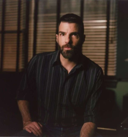 Portrait of Zachary Quinto with a short beard wearing a dark striped button-down shirt indoors against window blinds.