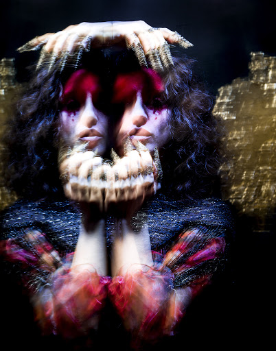 Woman with dramatic makeup and mirrored reflections in a blurred studio shot against a dark background.