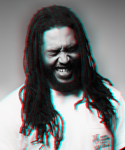 Close-up of a man with dreadlocks, eyes closed and mouth open, in a white shirt against a grey background with color distortion.