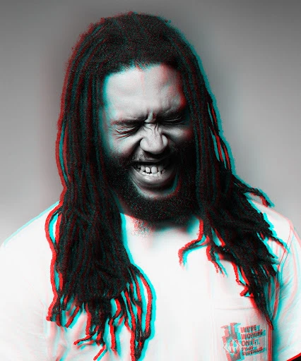 Close-up of a man with dreadlocks, eyes closed and mouth open, in a white shirt against a grey background with color distortion.