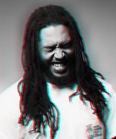 Close-up of a man with dreadlocks, eyes closed and mouth open, in a white shirt against a grey background with color distortion.