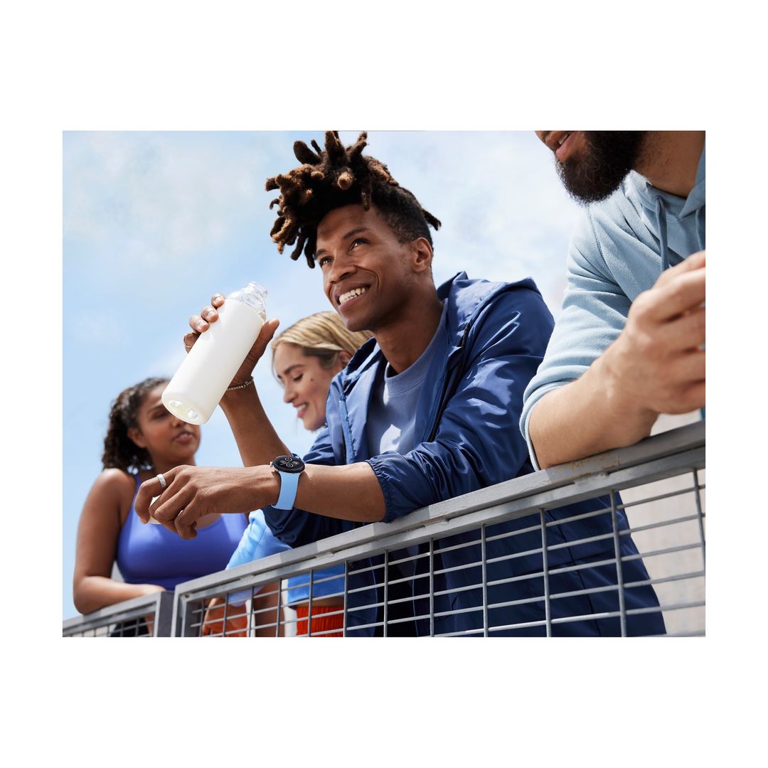 Group of diverse young adults leaning on a metal balcony railing against a clear sky, holding a water bottle.