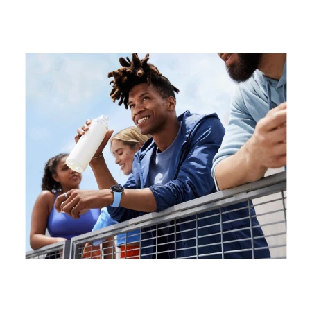 Group of diverse young adults leaning on a metal balcony railing against a clear sky, holding a water bottle.