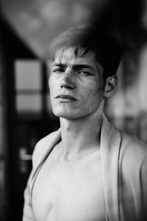 Portrait of a young man with dark hair and freckles wearing an open robe against an out-of-focus background.