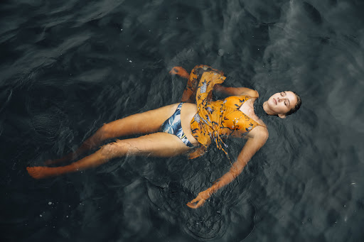 Woman in swimwear and yellow cover-up floating on her back in dark water with eyes closed, creating a serene and tranquil scene.