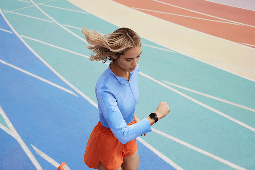 Woman in athletic wear runs on a colorful track, checking her smartwatch, showcasing a fitness lifestyle on a vibrant, modern background.