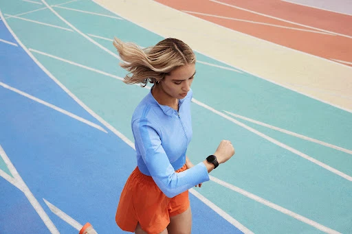 Woman in athletic wear runs on a colorful track, checking her smartwatch, showcasing a fitness lifestyle on a vibrant, modern background.