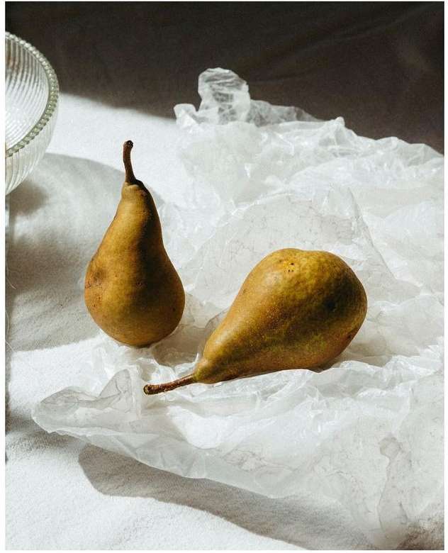 Two pears, one upright and the other lying on its side, are displayed on crumpled white paper, with a portion of a clear bowl visible.