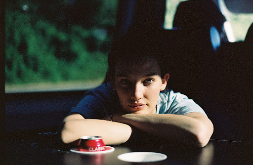 Portrait of a young adult looking directly at the camera with arms resting on a table with a can and saucer in an indoor setting.