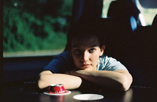 Portrait of a young adult looking directly at the camera with arms resting on a table with a can and saucer in an indoor setting.