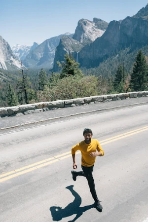 Athletic Black man in yellow shirt running on asphalt road with mountain landscape background on sunny day, fitness and outdoor activity.