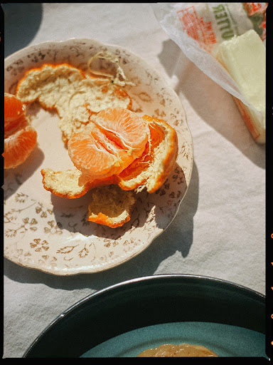 Overhead shot of a peeled mandarin orange on a decorated plate atop a white tablecloth, next to a package of butter.