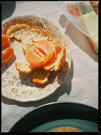 Overhead shot of a peeled mandarin orange on a decorated plate atop a white tablecloth, next to a package of butter.