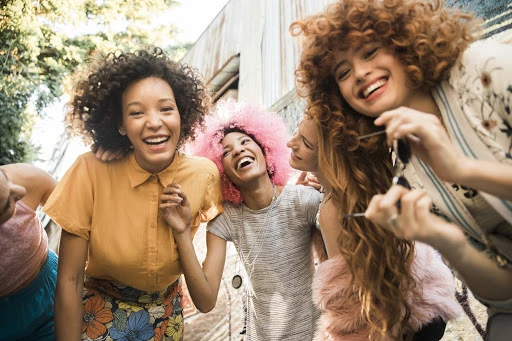 Group of diverse young women smiling together in an outdoor urban setting captured from a low angle by Emily Winiker.