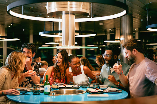 Group of six adults joyfully dining at a round table in a restaurant, featuring Korean Soju drink, plates, and dining accessories.
