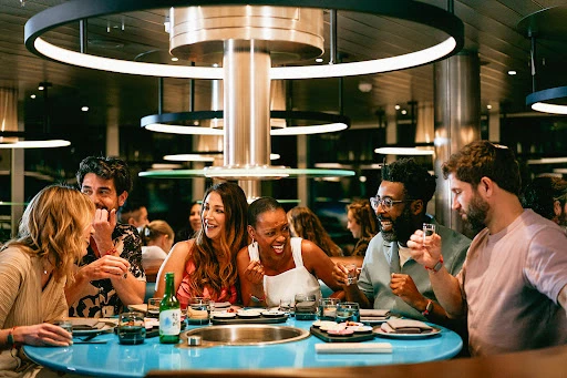 Group of six adults joyfully dining at a round table in a restaurant, featuring Korean Soju drink, plates, and dining accessories.