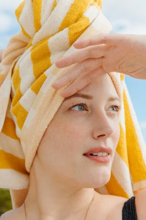 Close-up portrait of a woman with a yellow and white striped towel wrapped around her head against a bright sky