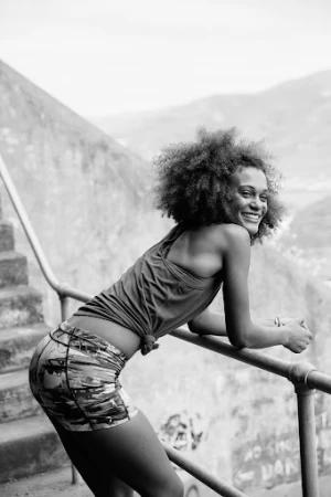 Black and white portrait of a smiling woman with curly hair leaning on a railing outdoors