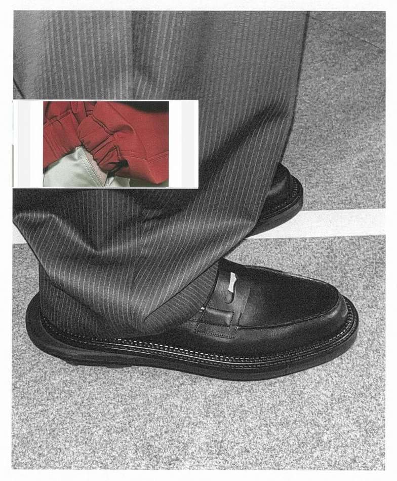 Close-up of a person's legs wearing pinstripe trousers and black loafers on a gray carpet, with an inset image of red fabric.