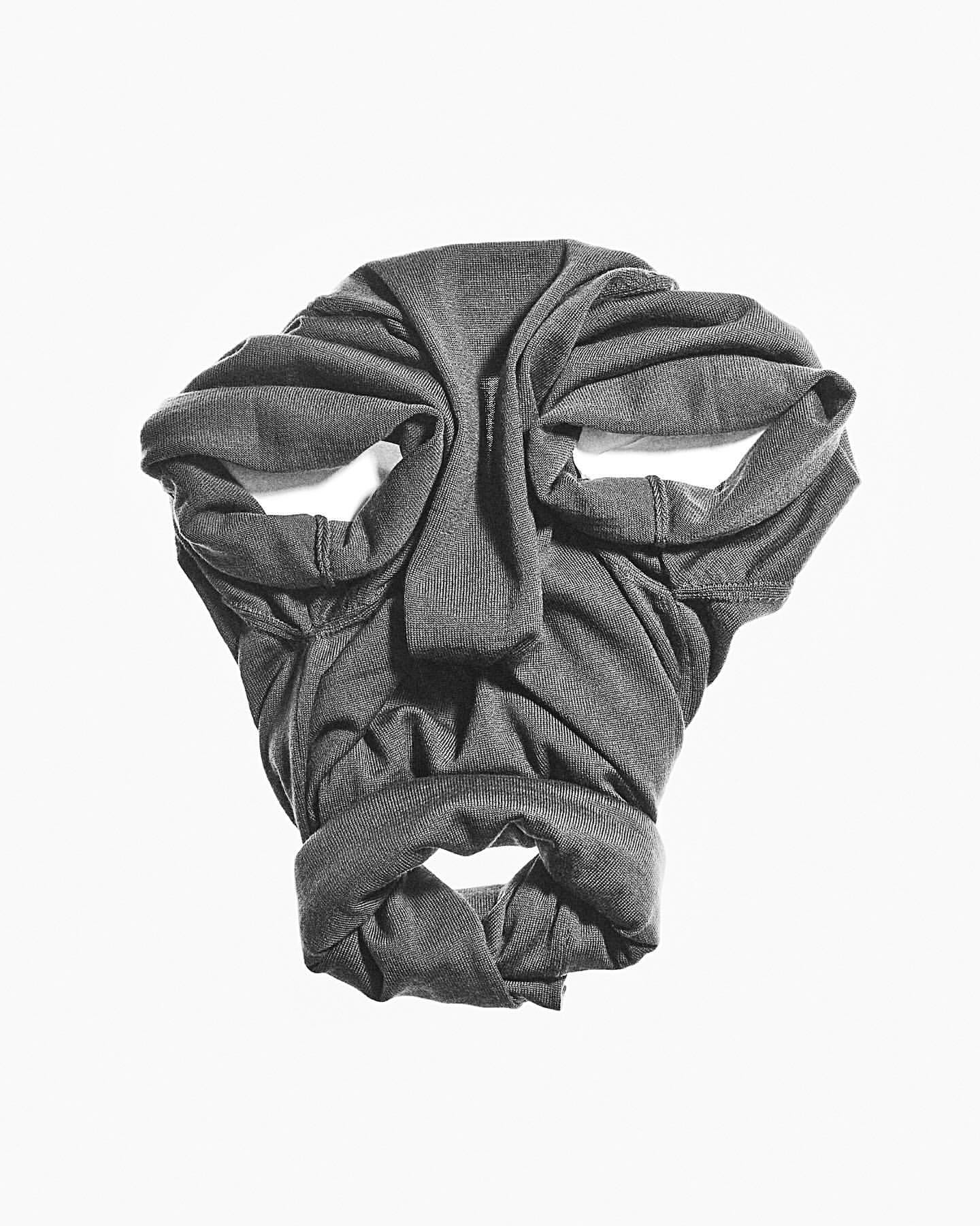 Folded gray shirt creates a face-like pattern on white background. Close-up studio shot of apparel artfully arranged to resemble features.