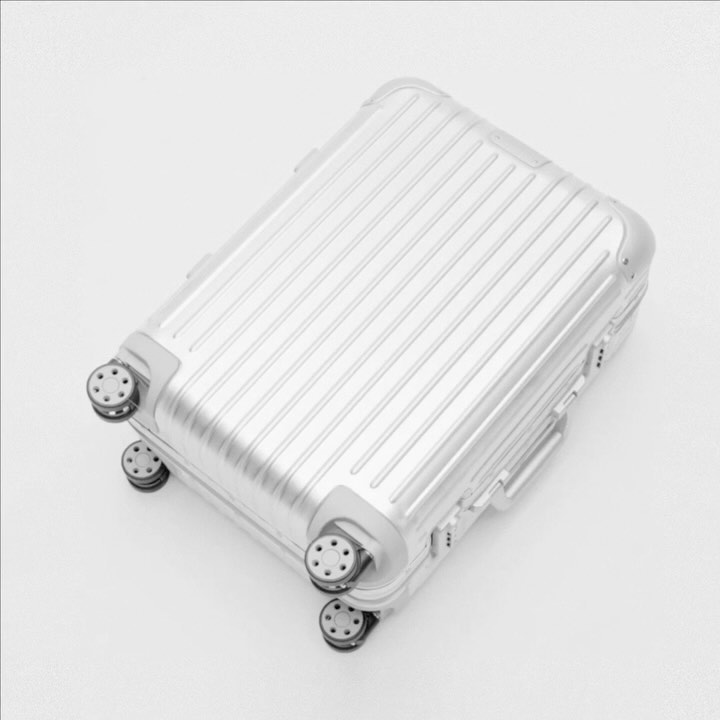 Overhead shot of a silver ridged carry-on suitcase with four wheels on a white background, suitable for travel or luggage concepts.