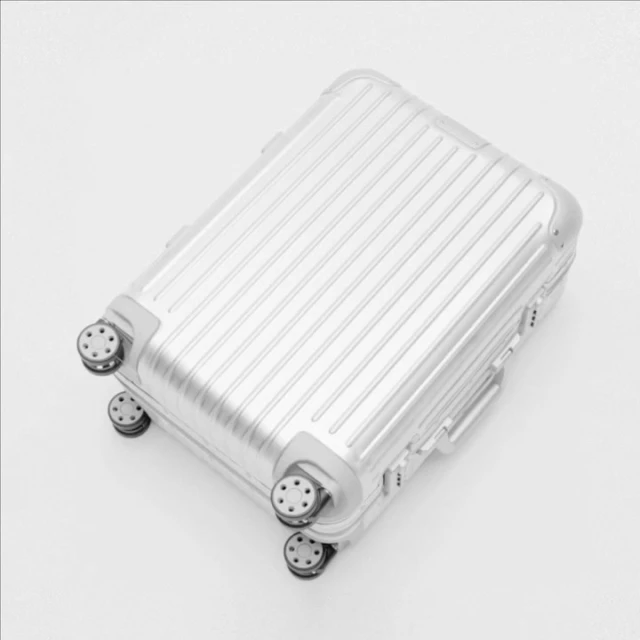 Overhead shot of a silver ridged carry-on suitcase with four wheels on a white background, suitable for travel or luggage concepts.