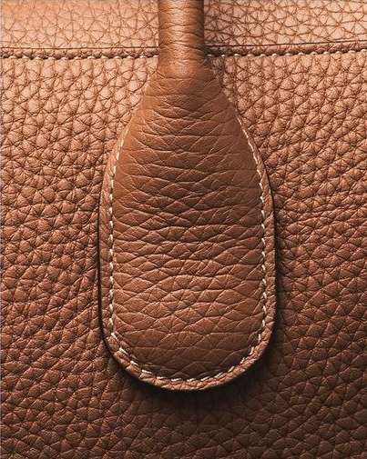 Close-up of brown leather bag with textured surface and handle, highlighting the material's details and craftsmanship.