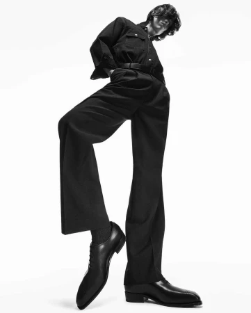Low angle monochrome fashion photograph of a male model in a dark shirt and trousers against a white seamless background