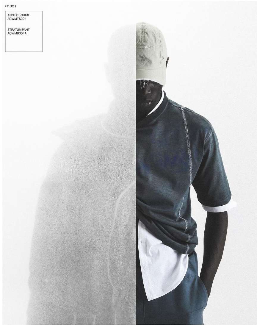 Fashionable dark-skinned man posing in a studio wearing a cap, navy shirt and pants, and white undershirt with a textured backdrop.