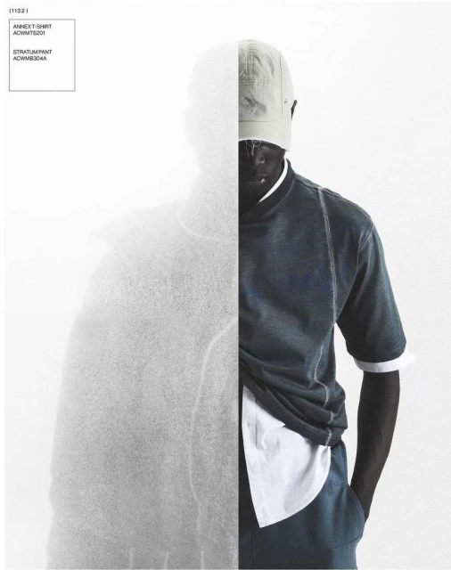 Fashionable dark-skinned man posing in a studio wearing a cap, navy shirt and pants, and white undershirt with a textured backdrop.