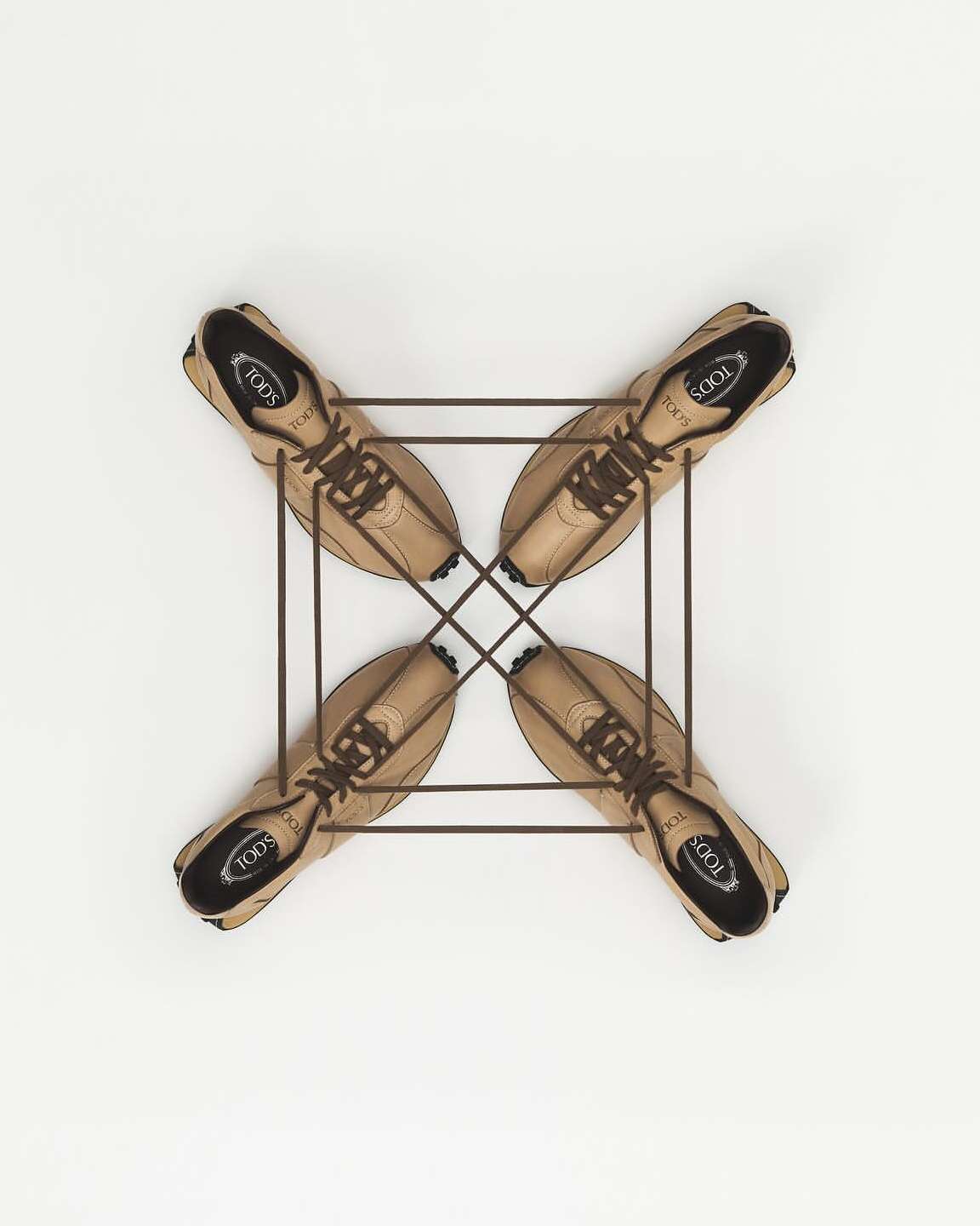 Overhead shot of tan leather Tod's loafers arranged in a radial pattern with a bronze-colored metal frame on a white surface.